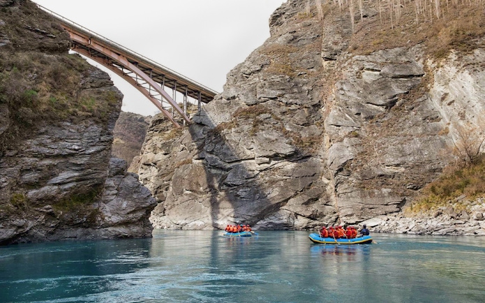Rafting on Kawarau River with bridge and rocky cliffs in background.