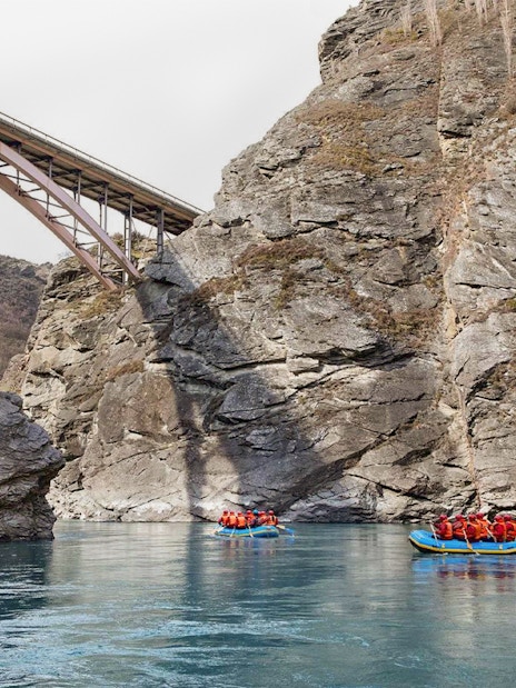 Rafting on Kawarau River with bridge and rocky cliffs in background.