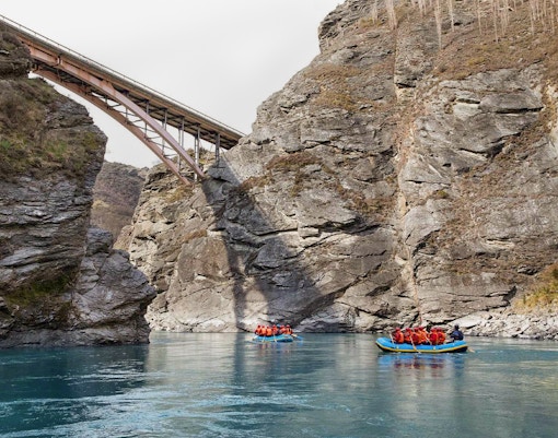 Rafting on Kawarau River with bridge and rocky cliffs in background.