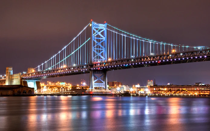 Ben Franklin Bridge illuminated at night over the Delaware River in Philadelphia.