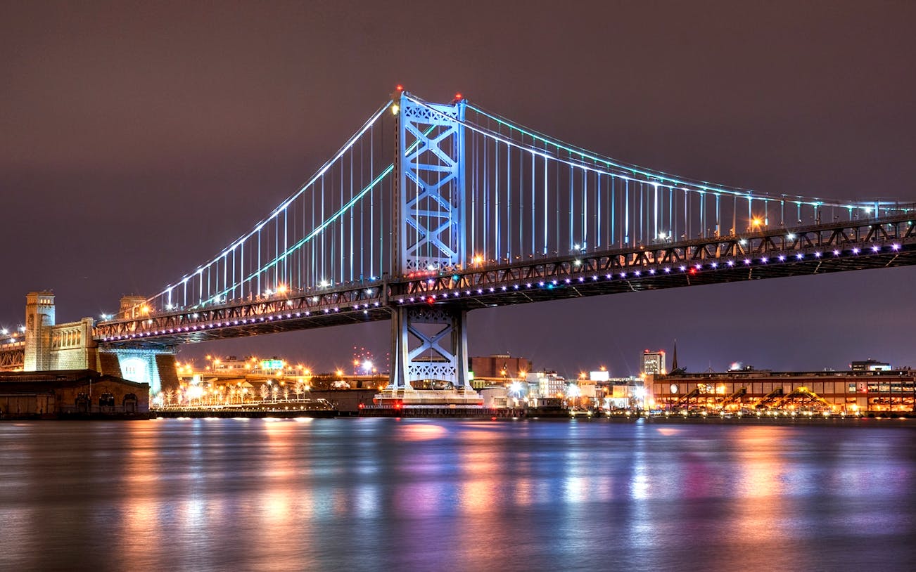 Ben Franklin Bridge illuminated at night over the Delaware River in Philadelphia.