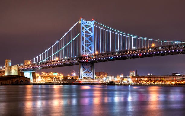 Ben Franklin Bridge illuminated at night over the Delaware River in Philadelphia.