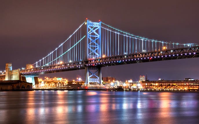 Ben Franklin Bridge illuminated at night over the Delaware River in Philadelphia.