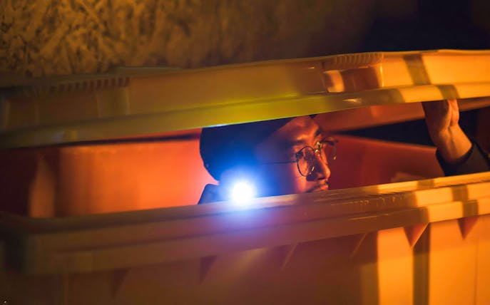 Person hiding in a container with a flashlight during Malaysia Breakout The Curve Spy Game.