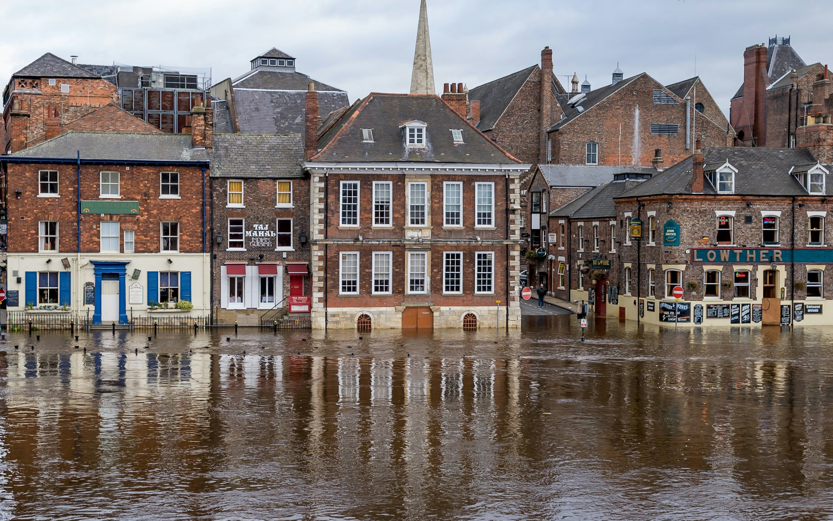 Flooded street view of King's Staith, York, with historic brick buildings and rising river water.