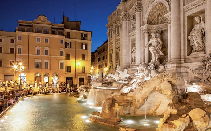 Trevi Fountain illuminated at night with surrounding buildings in Rome, Italy.