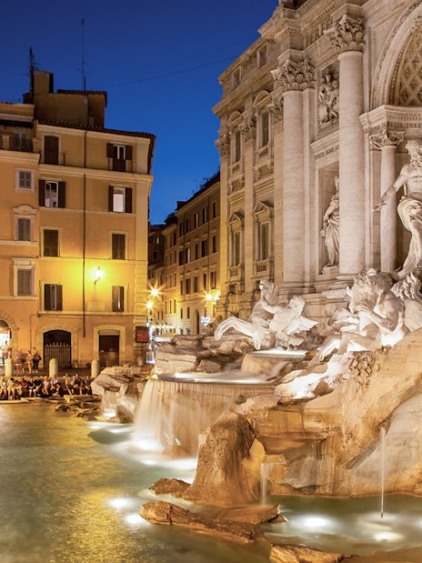 Trevi Fountain illuminated at night with surrounding buildings in Rome, Italy.