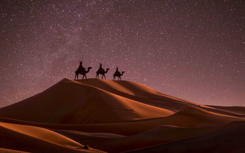 Camel riders on sand dunes under starry sky, Doha desert safari.