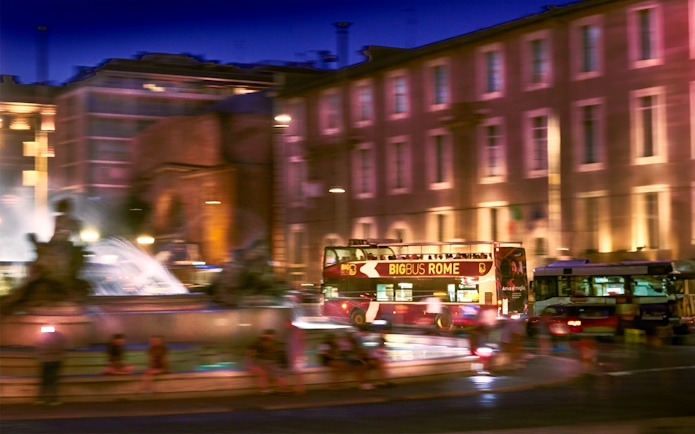 Big Bus tour passing by a fountain in Rome at night.