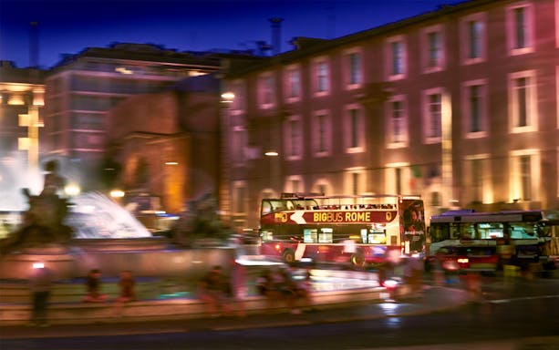 Big Bus tour passing by a fountain in Rome at night.
