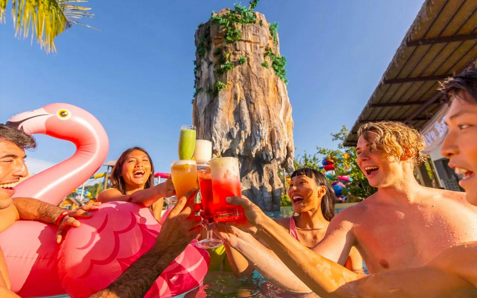Group enjoying drinks in the pool at Andamanda Phuket Water Park with a rock formation in the background.