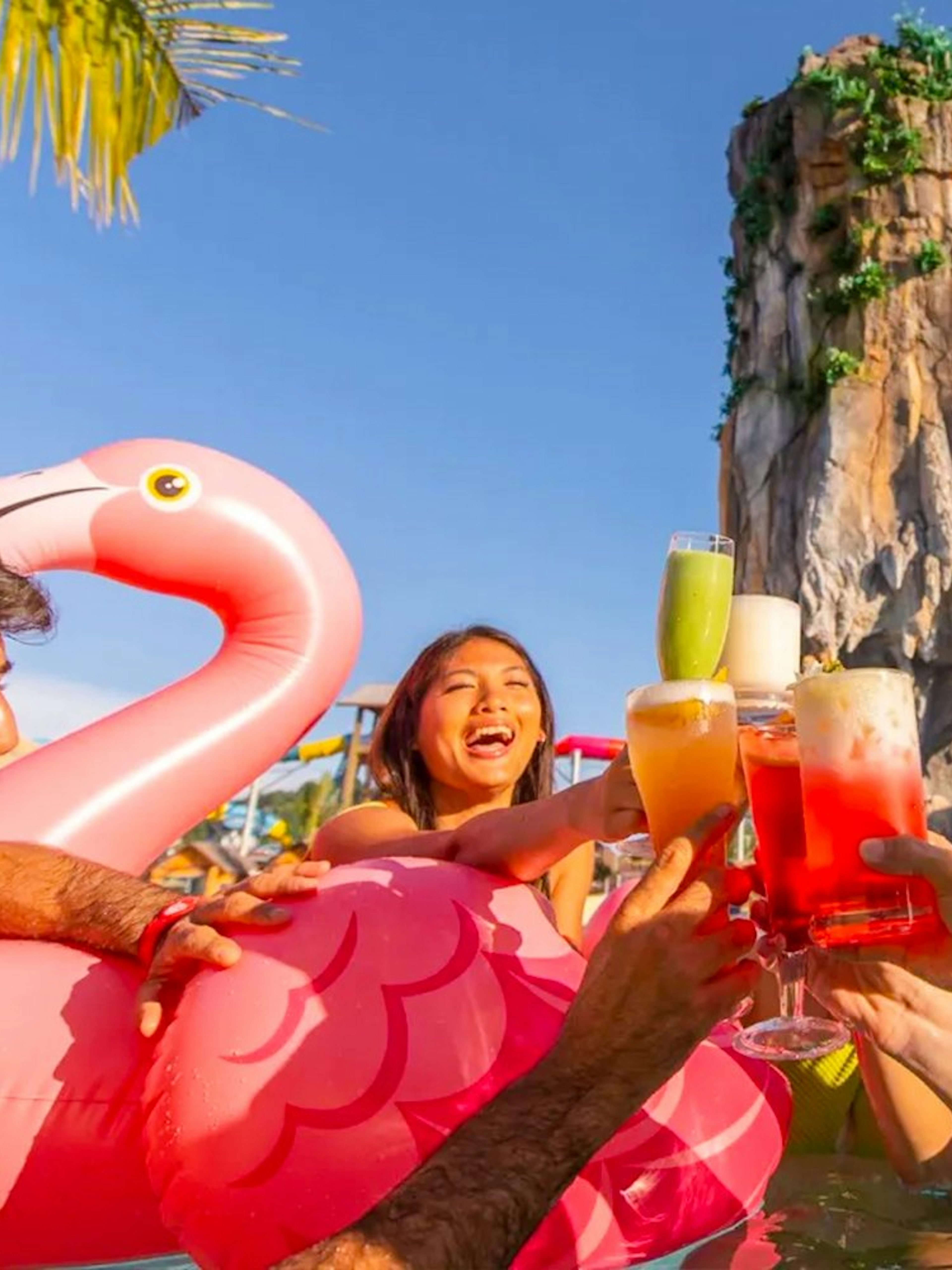 Group enjoying drinks in the pool at Andamanda Phuket Water Park with a rock formation in the background.