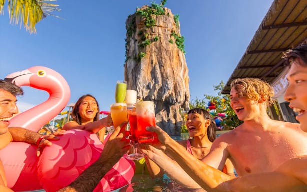 Group enjoying drinks in the pool at Andamanda Phuket Water Park with a rock formation in the background.