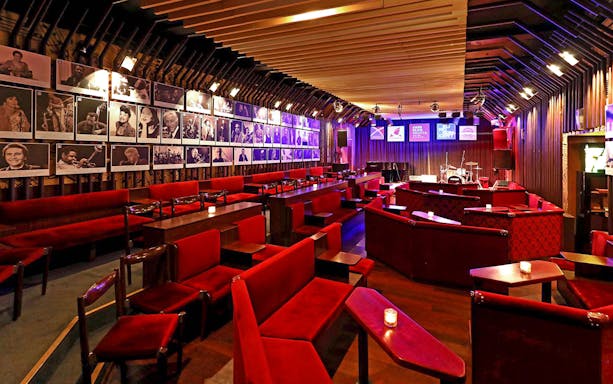 Interior of Reduta Jazz Club with red seating, stage, and musician portraits on walls.