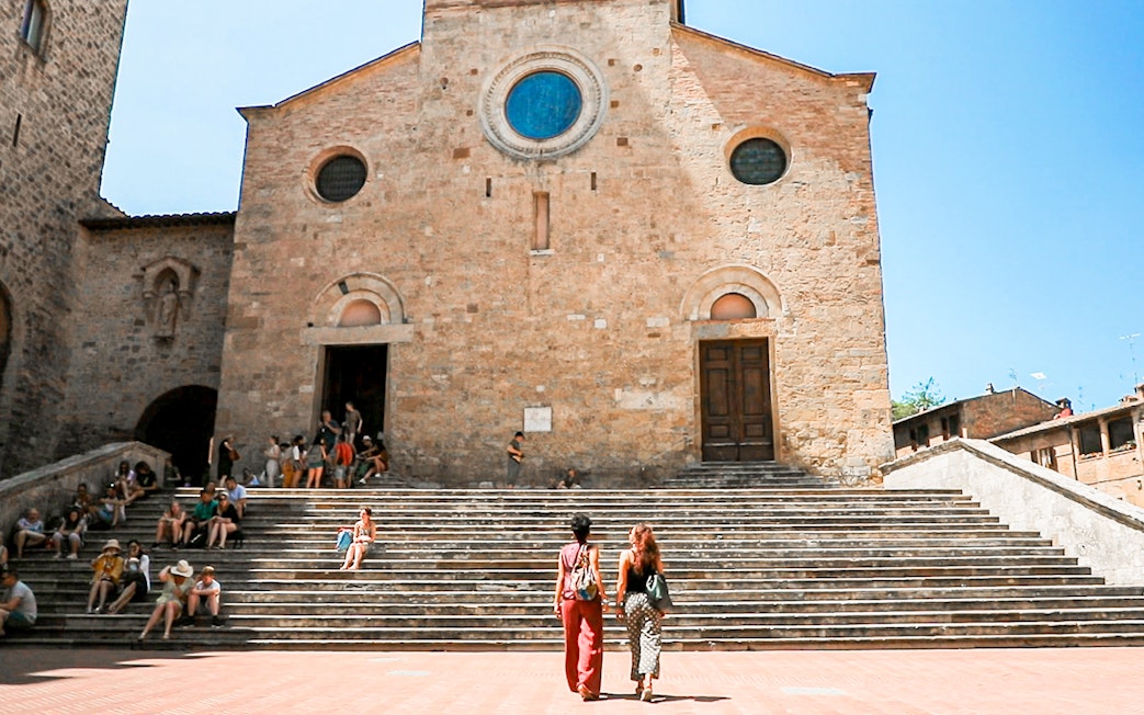 Visitors at the steps of a historic church in San Gimignano, Italy.