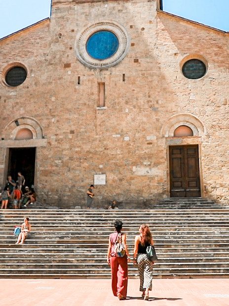 Visitors at the steps of a historic church in San Gimignano, Italy.