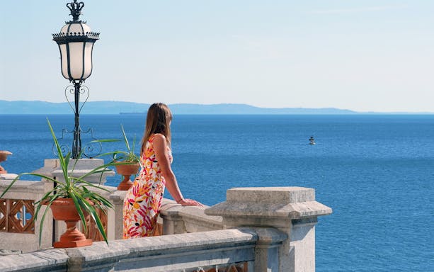 Woman on Miramare Castle balcony overlooking Adriatic Sea.
