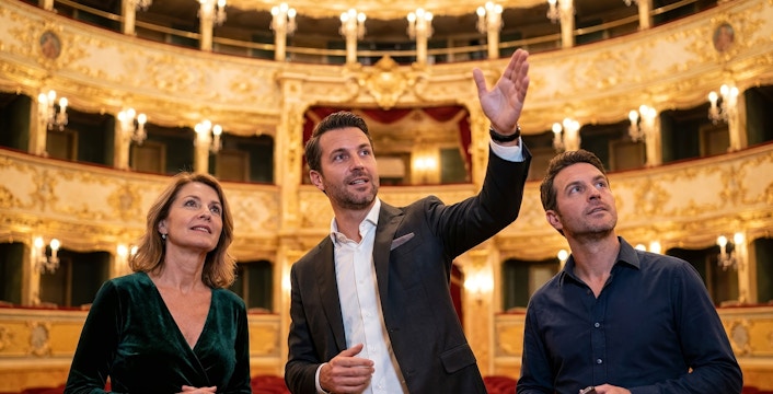 Tour guide with tourists inside Teatro La Fenice, Venice, pointing at ornate interior.