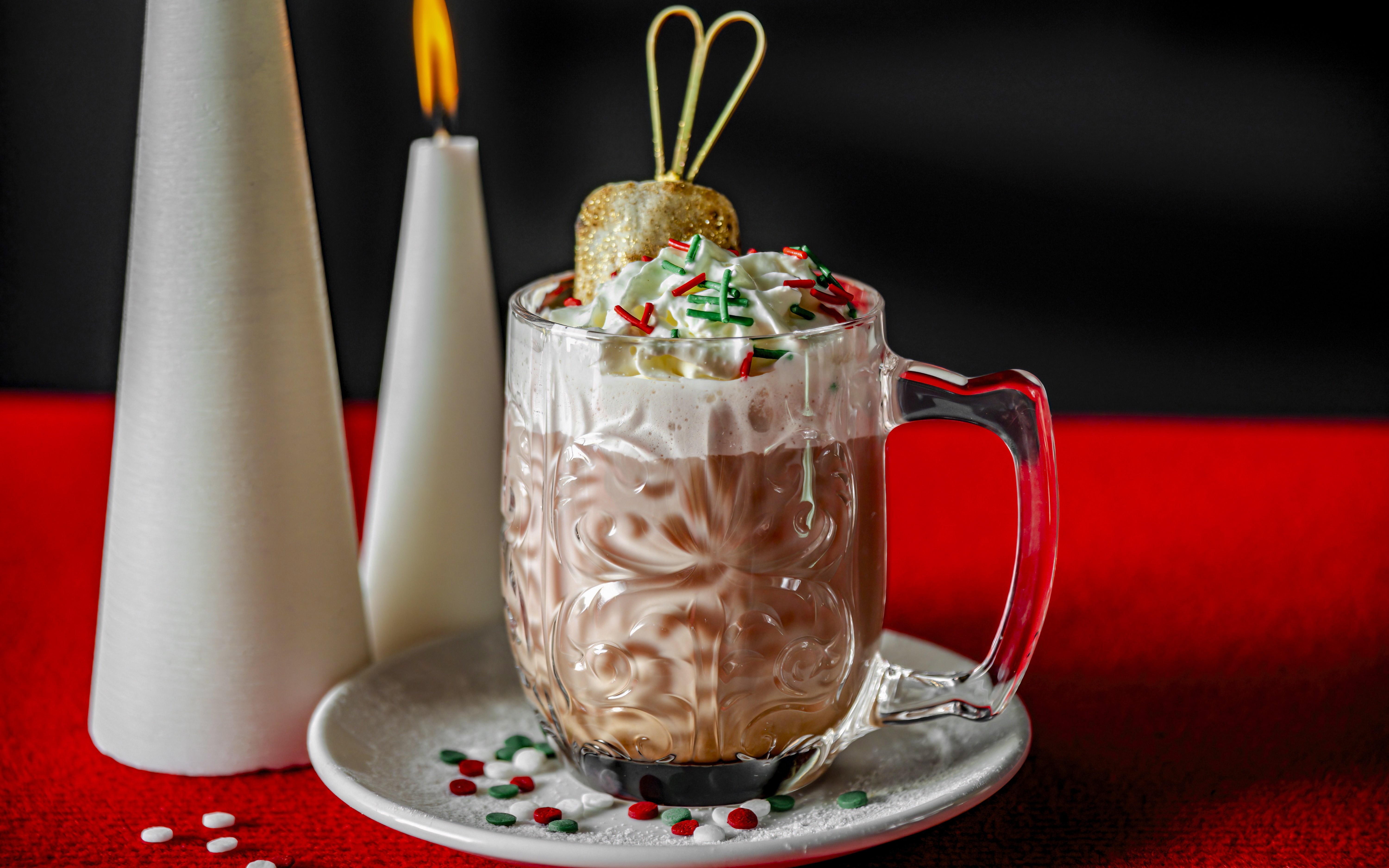 Festive hot chocolate with whipped cream and sprinkles on a red table.