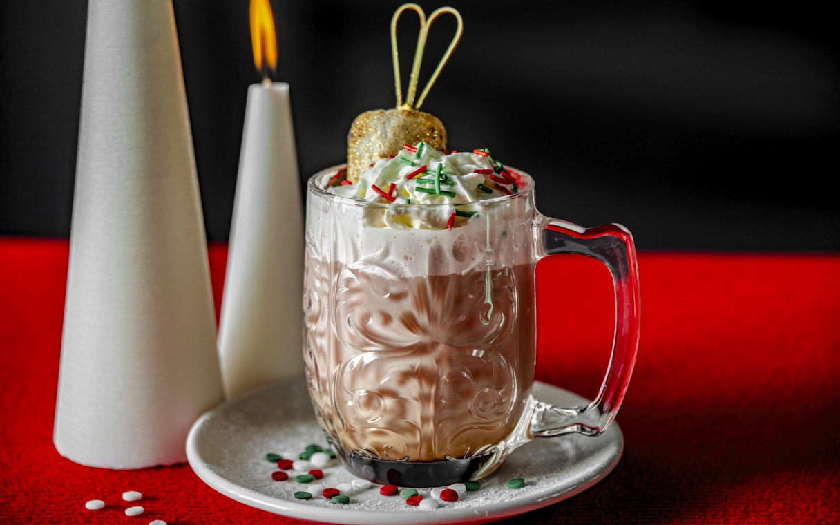 Festive hot chocolate with whipped cream and sprinkles on a red table.