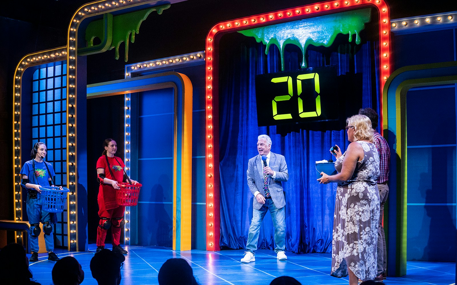 Game show set with host and contestants, featuring slime theme and digital timer reading 20.