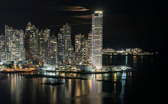 Panama City skyline at night with illuminated skyscrapers reflecting on the water.