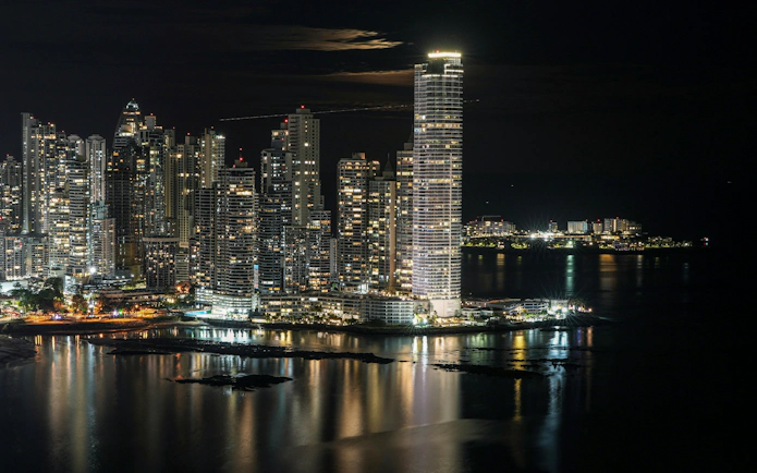 Panama City skyline at night with illuminated skyscrapers reflecting on the water.