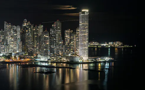 Panama City skyline at night with illuminated skyscrapers reflecting on the water.