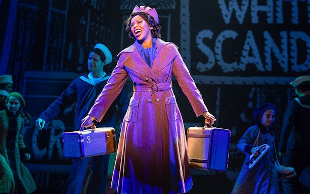 Performer on stage in a musical production of Annie, holding suitcases.