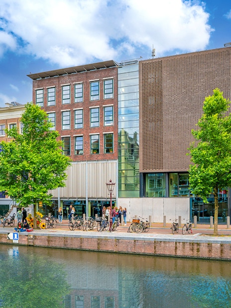 Anne Frank House exterior along Amsterdam canal with visitors and bicycles.