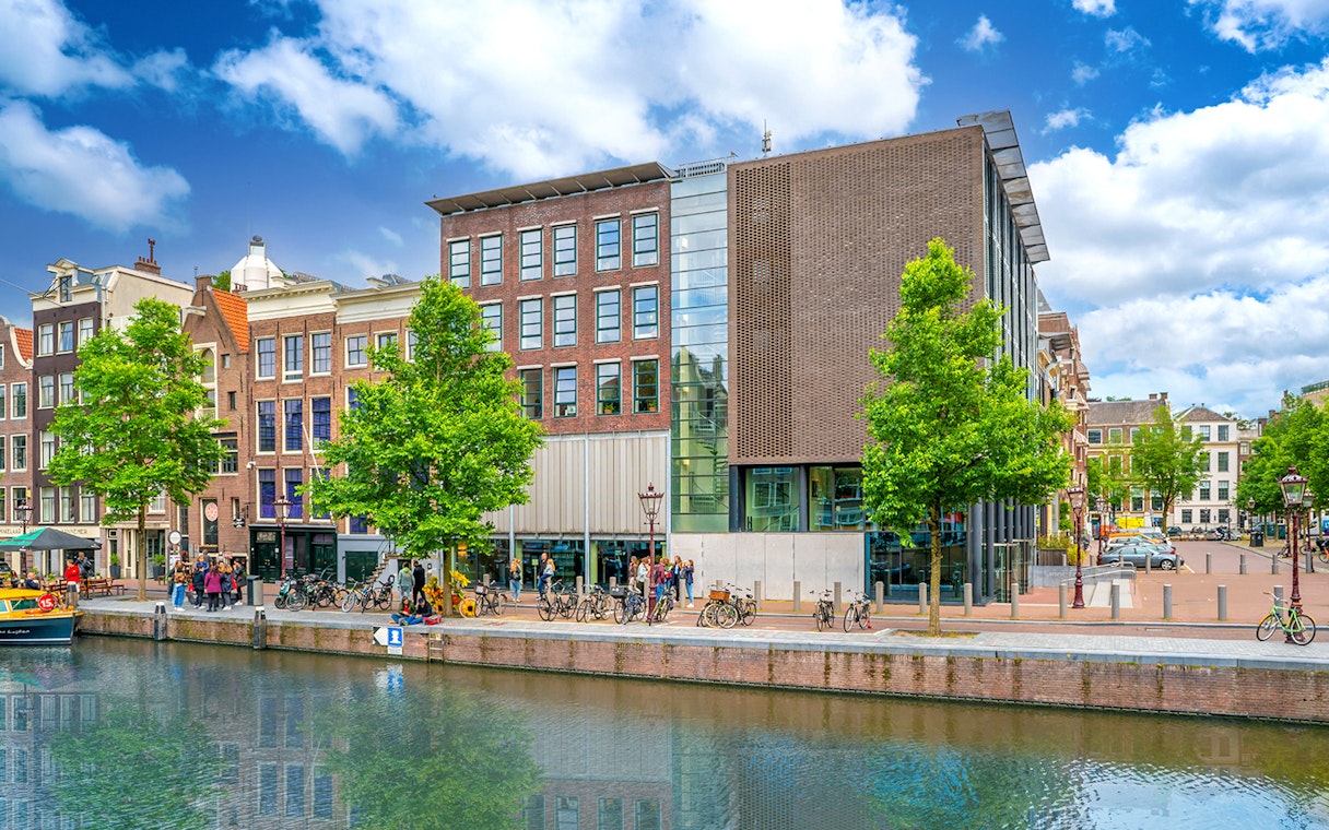 Anne Frank House exterior along Amsterdam canal with visitors and bicycles.