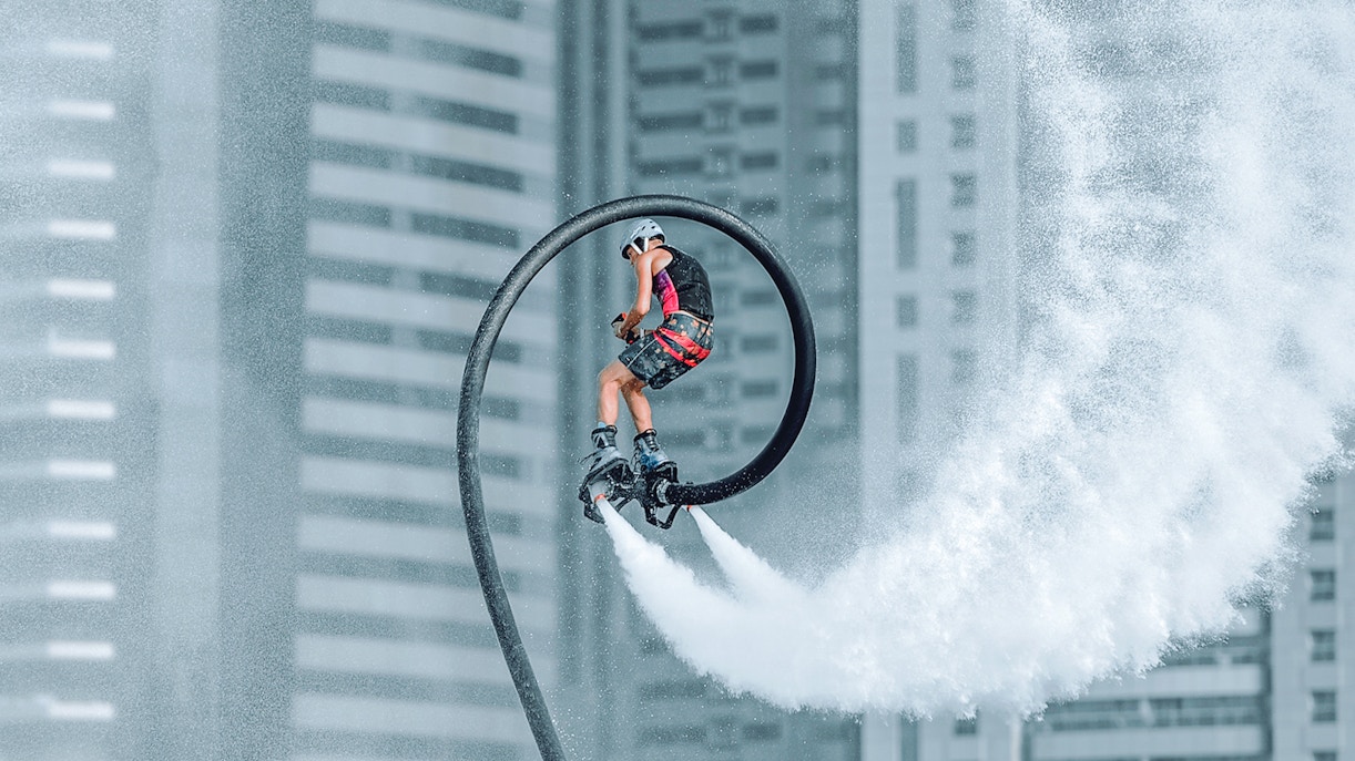 Person flyboarding with water jets in front of Dubai skyscrapers.