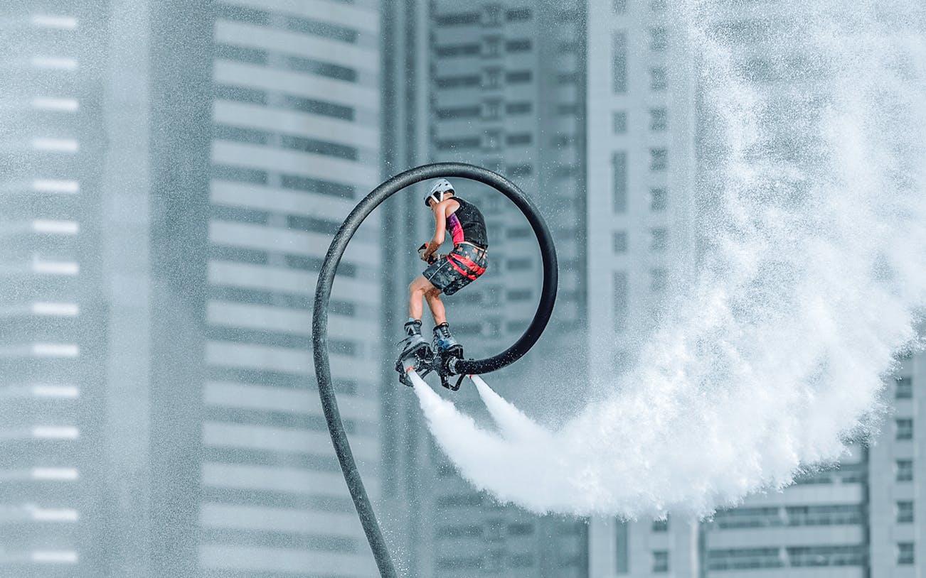 Person flyboarding with water jets in front of Dubai skyscrapers.