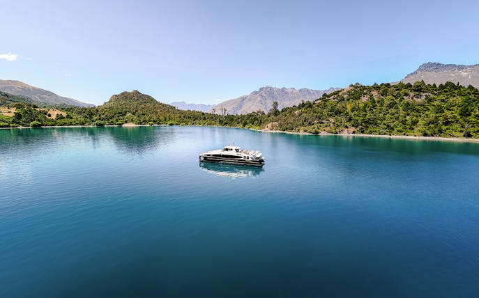 Boat cruising on Lake Wakatipu with snow-capped mountains in the background, Queenstown, New Zealand.