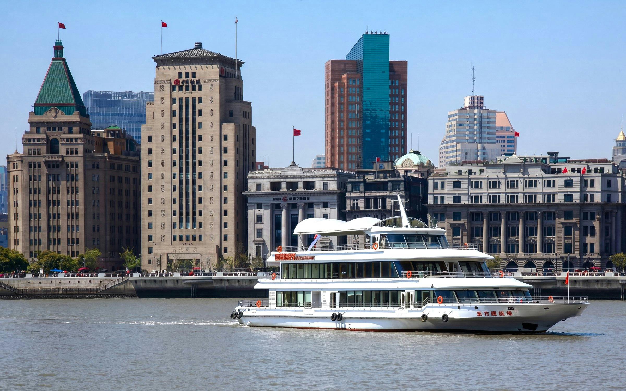 Huangpu River cruise boat passing Shanghai skyline with historic buildings.