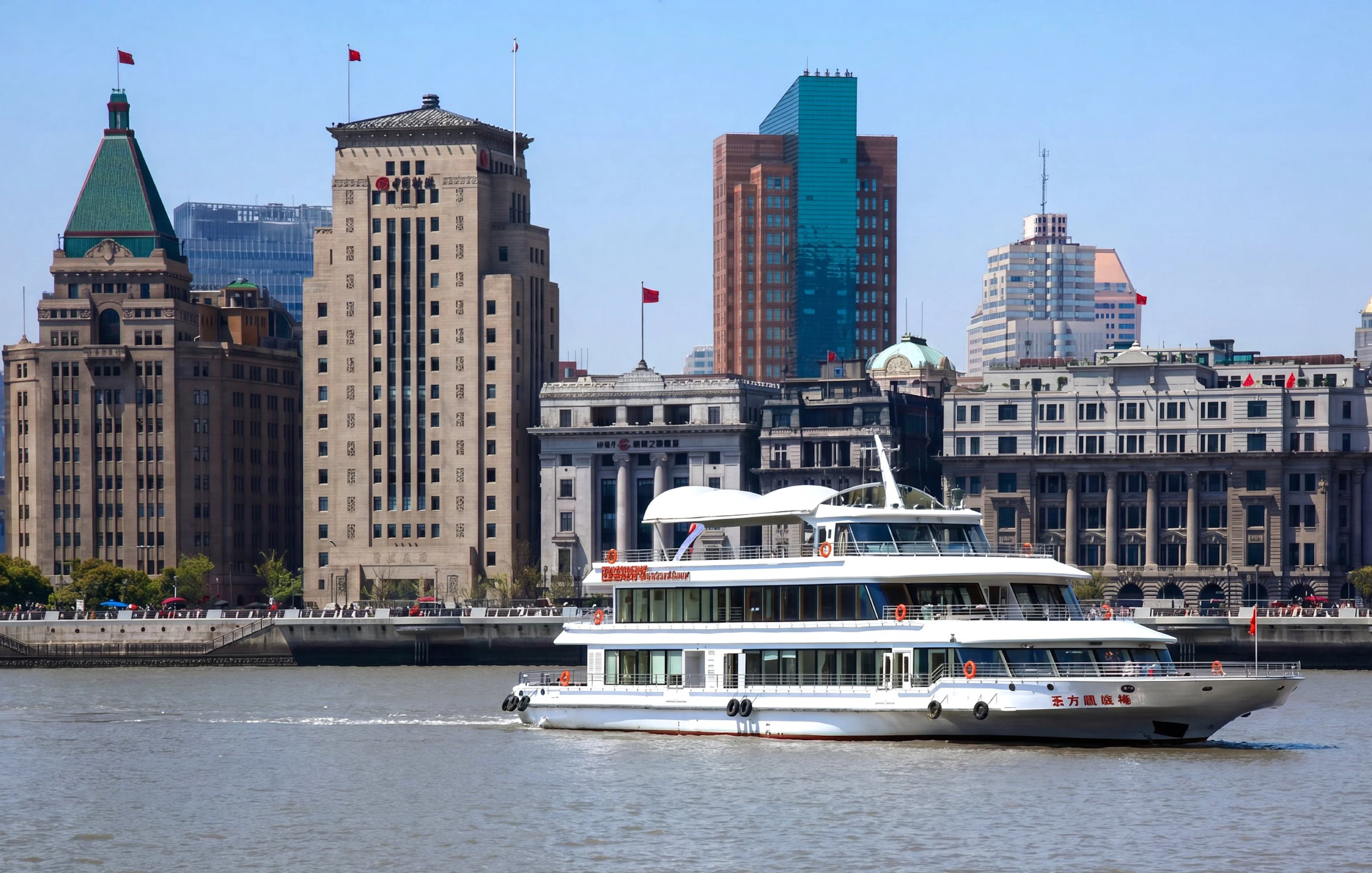 Huangpu River cruise boat passing Shanghai skyline with historic buildings.