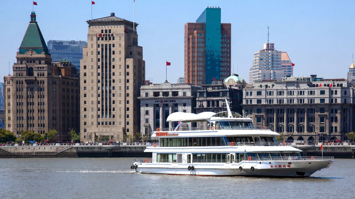 Huangpu River cruise boat passing Shanghai skyline with historic buildings.