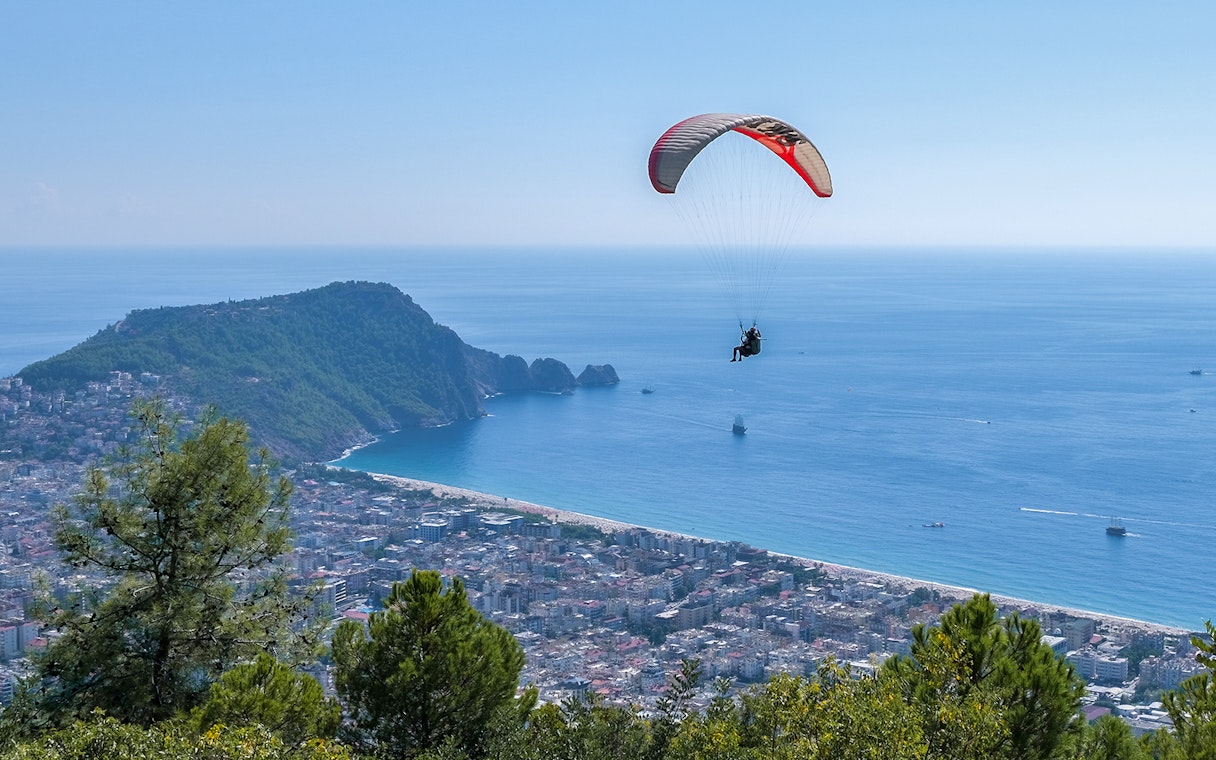 Paraglider soaring over Alanya coastline with city and sea view.