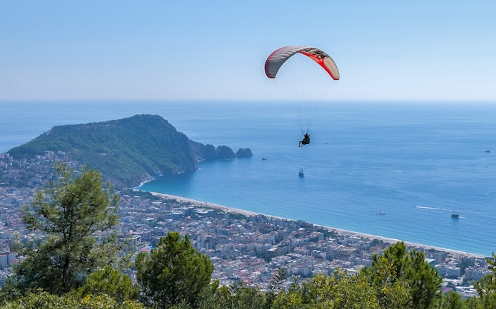 Paraglider soaring over Alanya coastline with city and sea view.