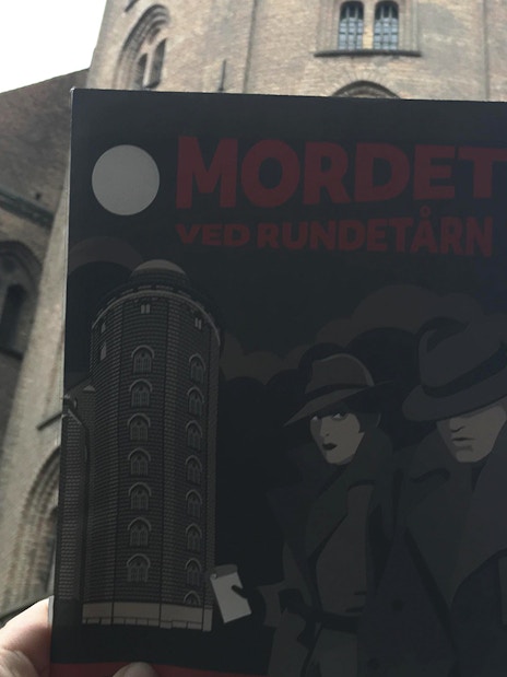 Murder Mystery Experience poster held in front of Round Tower, Copenhagen.