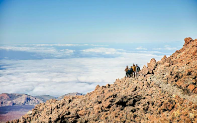 Group of hikers on rocky Mount Teide summit with clouds below, Tenerife.