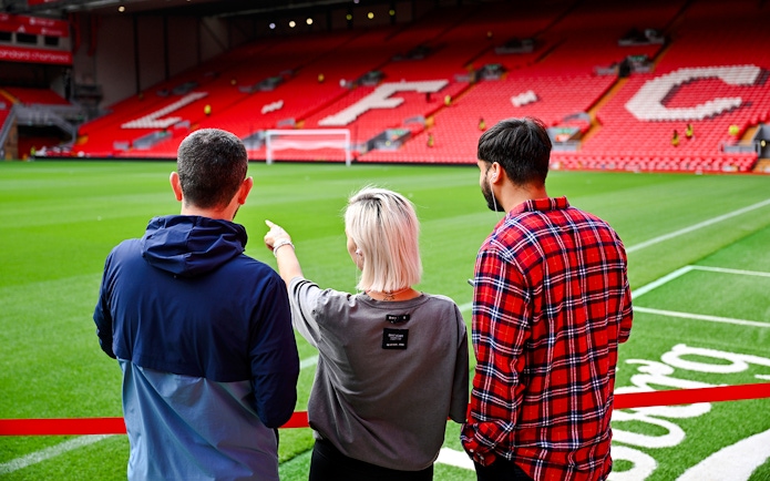 Visitors observing Anfield Stadium field during Liverpool FC tour.