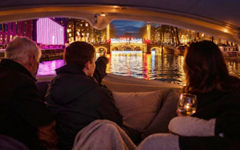 Boat tour during Amsterdam Light Festival with illuminated bridge and canal reflections.