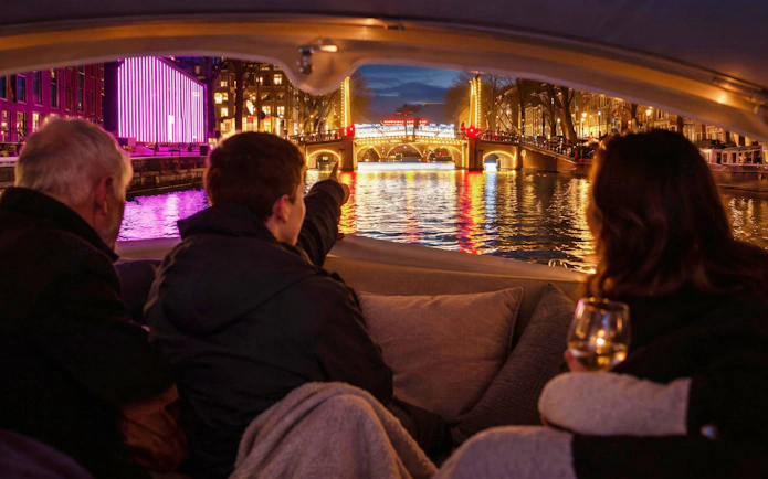 Boat tour during Amsterdam Light Festival with illuminated bridge and canal reflections.