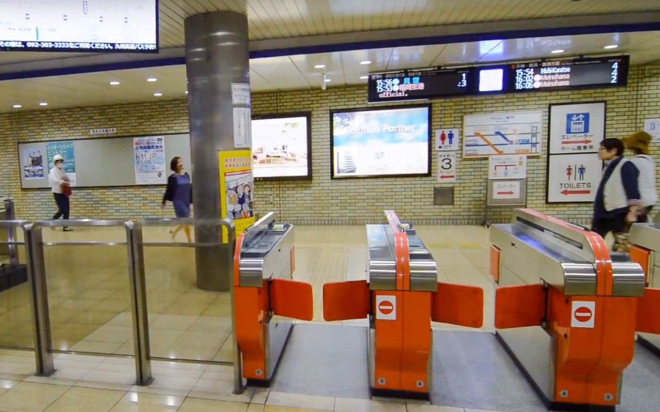 Fukuoka City subway turnstiles with passengers walking through station.