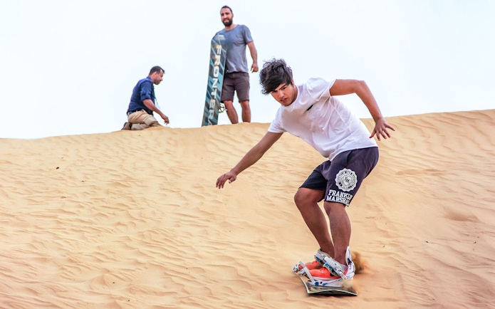 Sandboarding during sunrise desert safari with picnic breakfast.