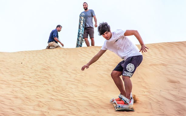 Sandboarding during sunrise desert safari with picnic breakfast.