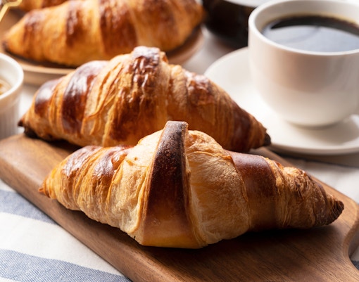 A croissant, and coffee and honey behind it in a cup