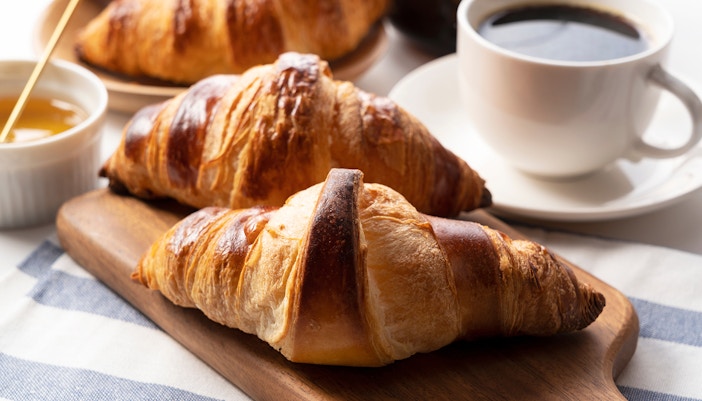 A croissant, and coffee and honey behind it in a cup