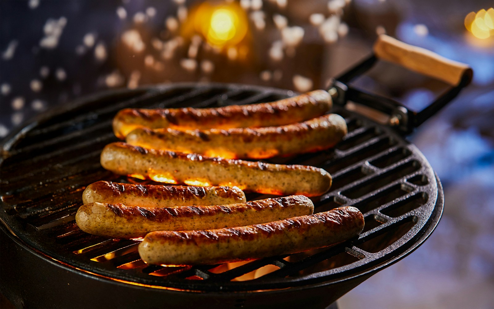Sausages grilling on barbecue at night with glowing coals.
